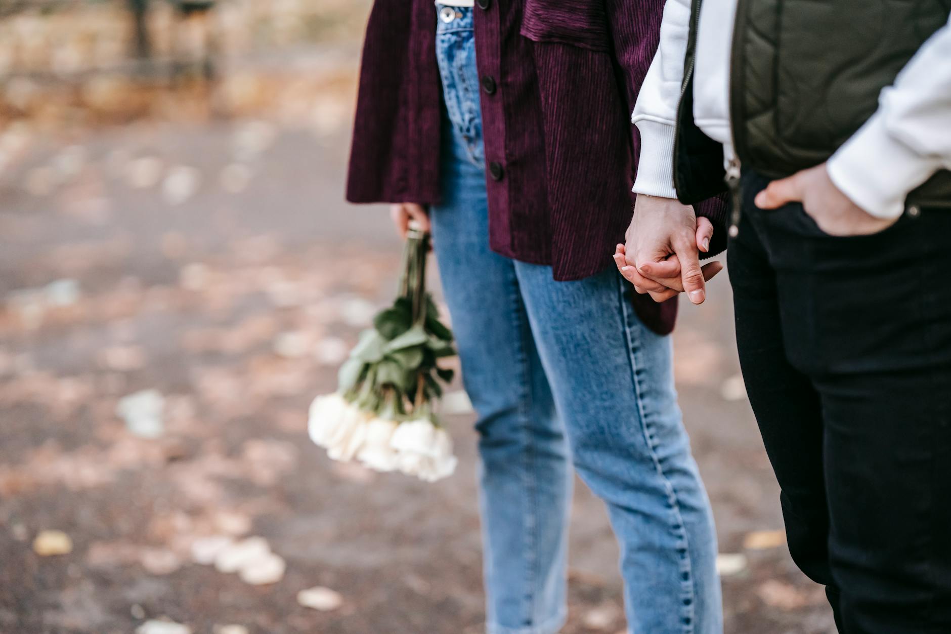 couple in casual outfit with bouquet of roses holding hands